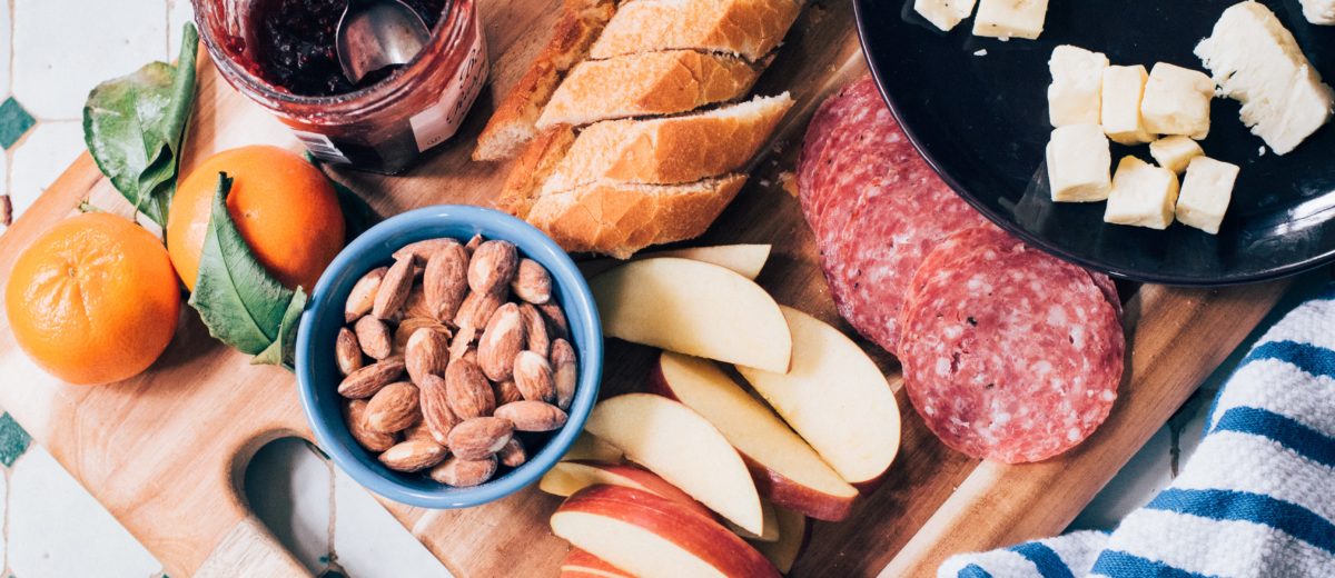 photo of a cutting board with cheese fruit nuts bread meat jam